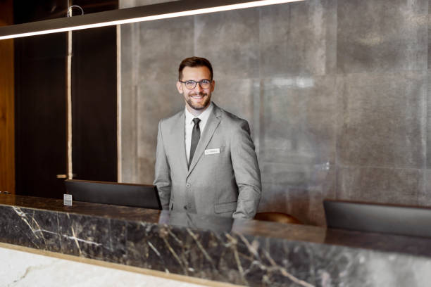 Male Receptionist Looking at Camera Attractive male receptionist looking at camera while working at the front at lobby desk hotel reception hotel service technology stock pictures, royalty-free photos & images