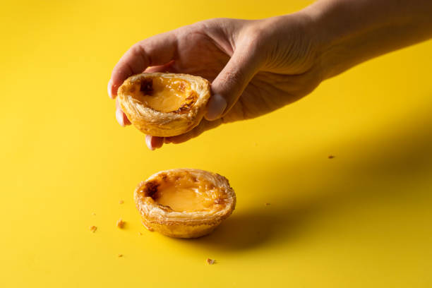mão feminina segurando doce típico português, pasteis de belem em backgorund amarelo - pastel de belem - fotografias e filmes do acervo