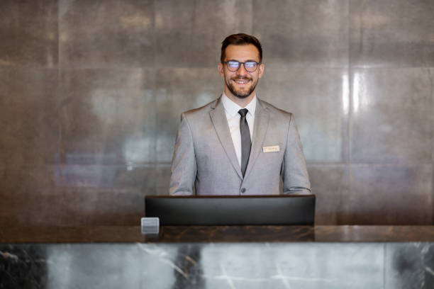Portrait of a young handsome Receptionist Attractive male receptionist looking at camera while working at the front at lobby desk hotel reception hotel service technology stock pictures, royalty-free photos & images