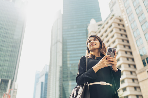 Confident Young Businesswoman With Smartphone Standing Against Modern Buildings