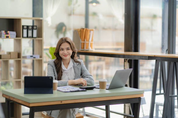 istock Female accountant working in financial accounting analyzing charts using laptop calculator with documents and holding pen with coffee cup in real estate office 1448296101