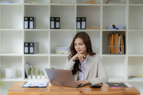 istock Female accountant working in financial accounting analyzing charts using laptop calculator with documents and holding pen with coffee cup in real estate office 1448296181