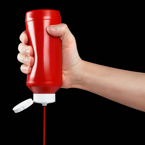 istock Hand squeezing ketchup out of a plastic bottle on black 1448298924