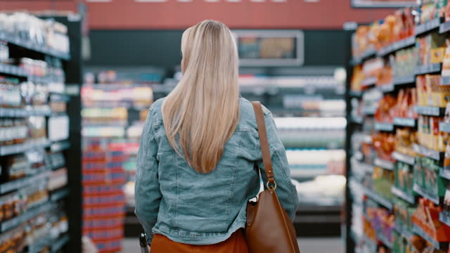 Woman, grocery shopping and supermarket aisle with shopping cart to buy food on sale in a retail store with discount. Female customer walking in shop for promotion product or groceries on shelf
