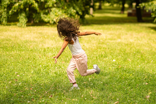 happy african american child outside, a girl in the park has fun, the child runs and plays, spinning in nature on a summer day,happy childhood
