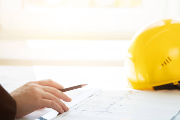 istock Architect working on blueprint, with architectural project at construction site at office, hard hat on engineering papers 1448307013