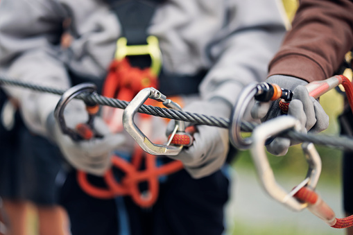 Teenage girl aged 16 with her brothers aged 13, wearing helmets and harnesses are training and practicing before the canopy tour in ropes course adventure park. They are learning to use the carabiners on the zip lines in a test location.
Canon R5
