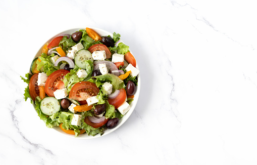 Greek salad with tomatoes, cucumbers, bell peppers, olives and feta cheese on a white background, copy space. Traditional Greek food top view.