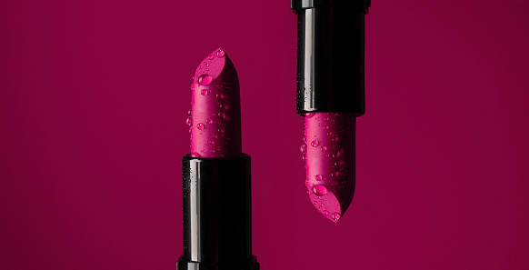 close-up on two red lipsticks in splashes of water on a red background