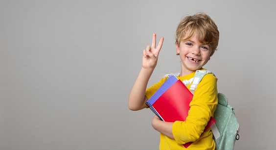 Primary school smiling boy girl over grey background with backpack and colorful exercise book showing thumbs up. Copy space for advertising blank concept. Back to school. Childhood, education, products for children