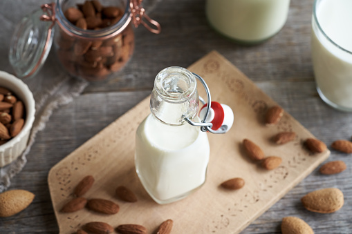 A bottle of vegan almond milk on a table, with whole almonds in the background