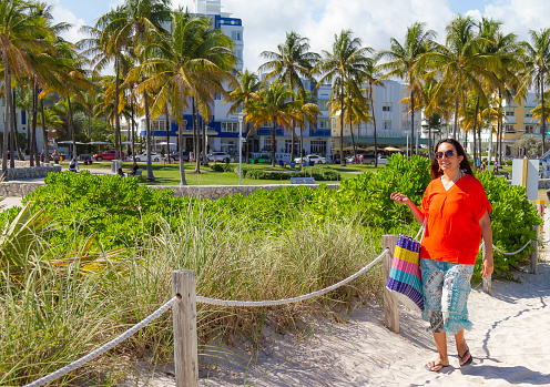 Young latin woman enjoying a day trip at the World famous Miami Beach, South Beach, Florida, United States of America, USA,  sunlight illuminating at midday on a blue sunny summer day. 

She's wearing a colorful orange shirt, a light blue skirt and sunglasses in a hot midday summer day.