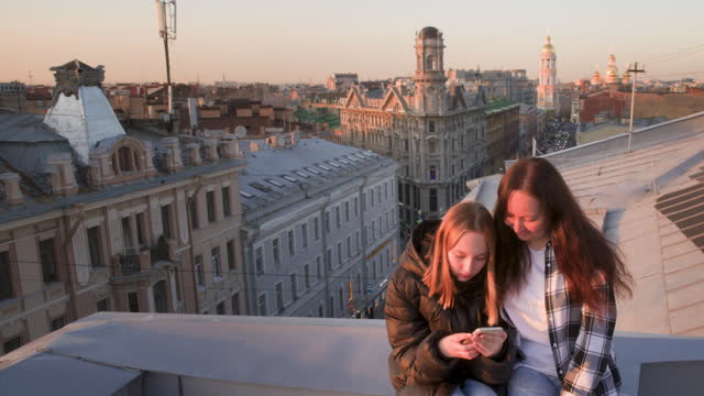Mom And Daughter Are Looking In Smartphone On The Roof Of Ancient Europe City.