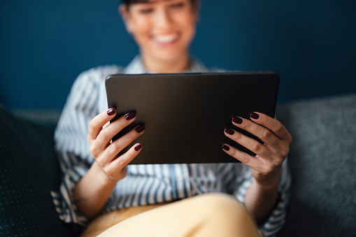 Close up of an unrecognizable woman sitting and holding a digital tablet.
