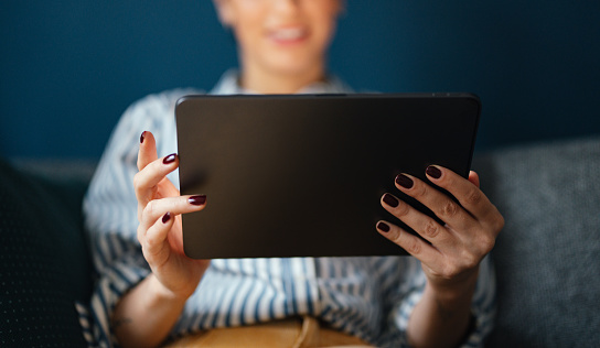 Close up of an unrecognizable woman sitting and holding a digital tablet.