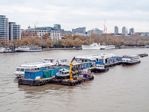 A group of floating platforms and barges used for boat maintenance, moored in the middle of the River Thames in Central London.