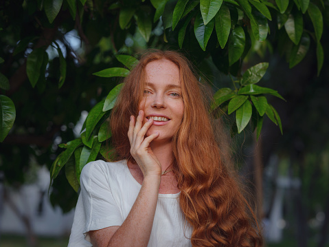 Beauty Woman Face With Healthy Skin And Green Plant at sunset time outdoor. Healthy lifestyle, beauty, natural concept. Melancholic beautiful portrait