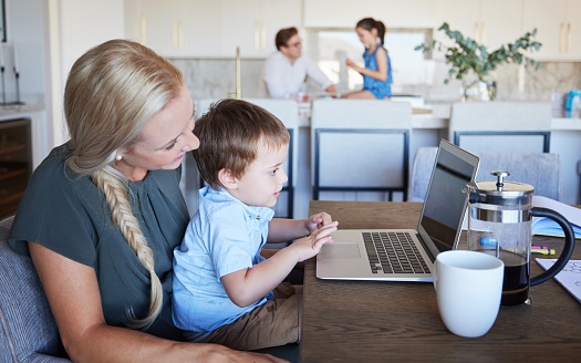 Mother, kid and laptop at table in living room with father and girl in background. Work from home mom on coffee break with son. Child development, family time and relax, a mothers love for children