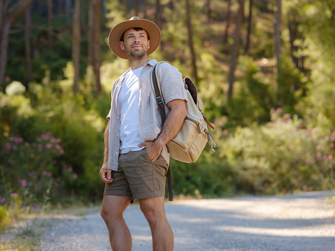 concept of embracing fresh air and engaging in outdoor activities. Man Traveler with backpack and hat hiking in mountains forest. Travel Summer Lifestyle concept.