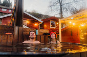 Happy woman and man relaxing in hot tub with scenic mountain view by the fjord in winter in Norway