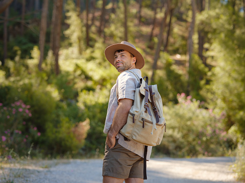 concept of embracing fresh air and engaging in outdoor activities. Man Traveler with backpack and hat hiking in mountains forest. Travel Summer Lifestyle concept.