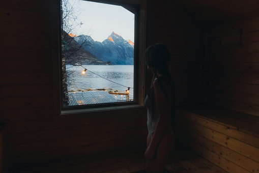 Silhouette of female with long hair contemplating the weekend by the sea with mountain view sitting in the sauna in Sunnmore Alps, Scandinavia