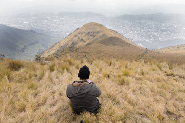 istock man admiring the landscape from a meadow on a mountain wears jacket clothes and wool cap, sitting on his back 1448345814