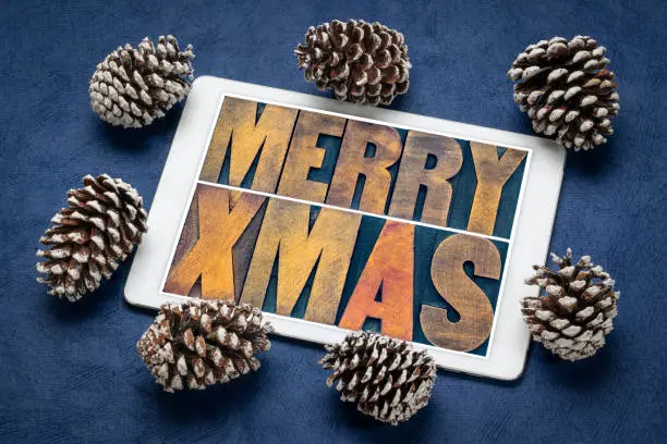 Merry Xmas (Christmas) greetings or wishes - word abstract in vintage letterpress wood on a digital tablet against blue bark paper, winter holidays banner