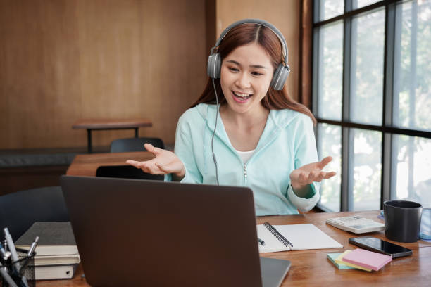 istock Female student in headphone is using laptop to asking question with teacher on video call while studying 1448355284
