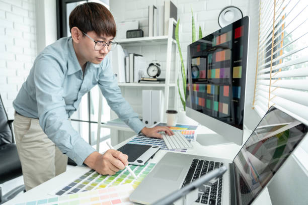 istock Male graphic designer is standing to choosing color swatch samples on multiple screens and working graphic design with technology while sketching on tablet digital in modern office 1448356352