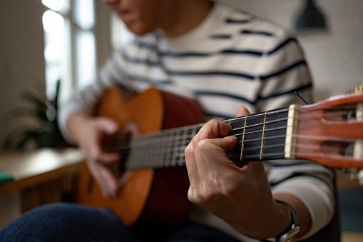 Close up of unrecognizable man playing a guitar at home.
