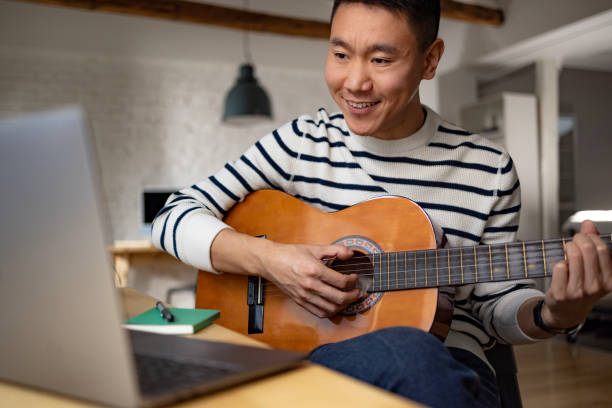 istock Happy Asian man teaching guitar lesson over laptop at home. 1448356583