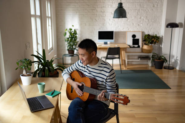 istock Happy Asian man playing acoustic guitar during e-learning from home. 1448356662