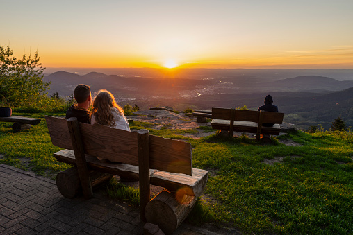 Visitors and lovers at the Devil's Mill in the Black Forest sit on benches and watch the sunset over the Murg and Rhine valley, Germany