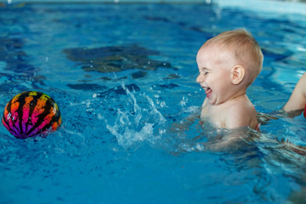 istock Little kid boy learns to swim and has fun in pool with mom support. Colored ball. 1448357199