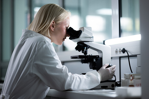 Profile view of young scientist analyzing medical sample through a microscope in laboratory.