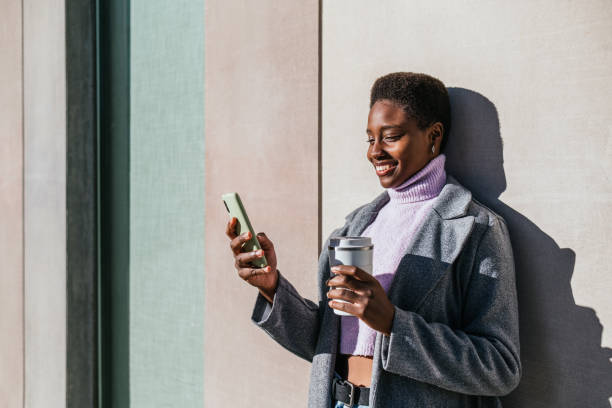 istock Black female with coffee and smartphone leaning on wall 1448358278