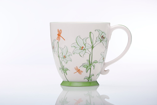 High angle view of a tea cup, a tea strainer with herbal tea in it and and flowers on a wooden table.