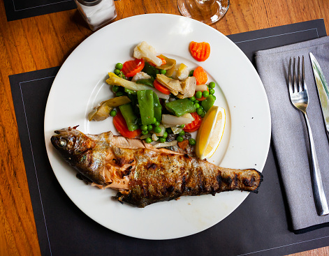 Appetizing grilled trout with stewed vegetables and a slice of lemon
