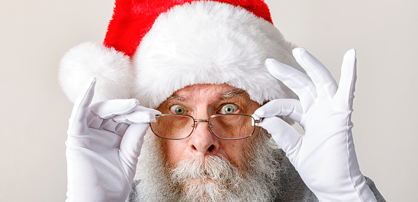 A curious, somewhat surprised looking Santa Claus is peering wide-eyed over his eyeglasses as he adjusts them while staring directing at the camera. Apparently he's not sure if YOU have been bad or good...!!