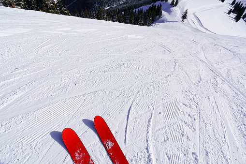 Dropping in to Vail Mountain Ski Slopes - POV view of skis and uncrowded ski slopes about to drop down onto ski run. Red skis on groomed slope with scenic views. Vail, Colorado USA.