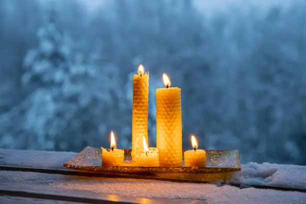 Set of natural rolled beeswax candles from pressed beeswax honeycomb sheet at home balcony outdoors snowy winter forest on background. Hobby concept. Lot of candles burning with copy space.