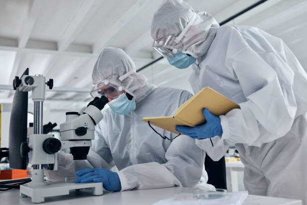 Scientist team, covid research and microscope with team writing notes or results during analysis of a sample in a science and medical lab. Medical researcher in safety suit in biotechnology laboratory equipo científico, investigación covid y microscopio con equipo escribiendo notas o resultados durante el análisis de una muestra en un laboratorio científico y médico. investigador médico en traje de seguridad en laboratorio de biotecnología
