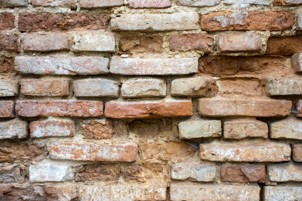 istock Old ancient brick wall with protruding bricks in brown and red tones, holes in the wall, fallen bricks and crumbling cement, symbolizing antiquity and the change of generations. For use as background 1448367379