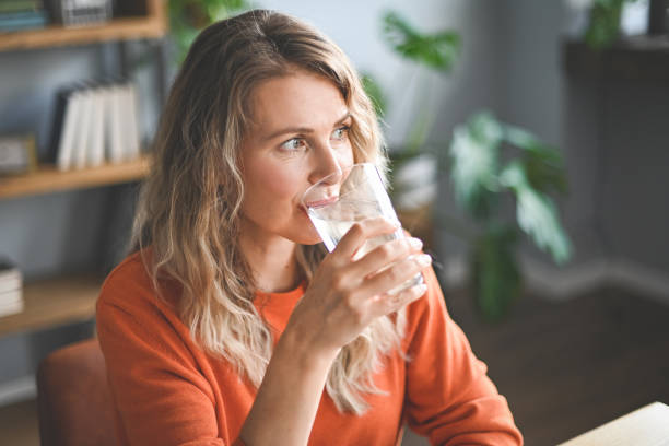 mature adult woman drinking water from a glass stock photo