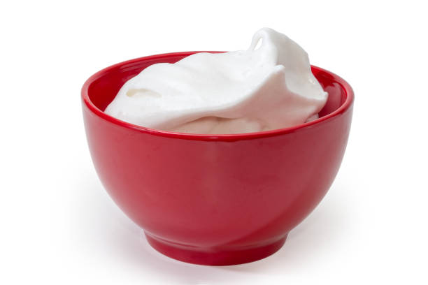 Beaten egg whites with sugar for dessert preparation in the red ceramic bowl on a white background