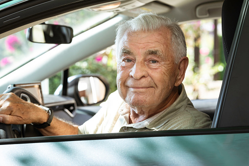 Senior in car is looking at camera with a warm smile.