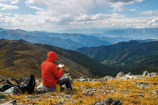 A man hiker studies a map of the area in his phone against the background of a beautiful mountain valley.