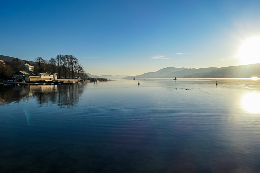 View on Woerthersee from Poertschach in Carinthia, Austria. Calm lake reflecting the landscape. View on the Karawanks Alps and Pyramidenkogel. Sunset sunrise vibes. Villages at the waters edge. Reed
