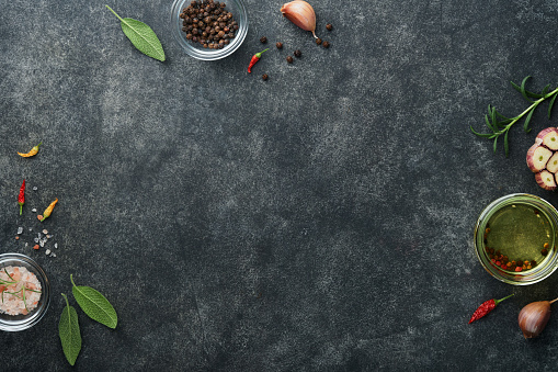 Food cooking background. Green rosemary branches, olive oil, garlic, peppercorns and hot peppers at dark slate concrete table. Food ingredients top view.